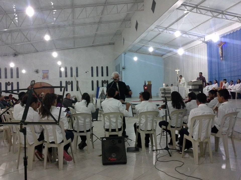 Orquestra jovem com camisetas verdes tocando durante missa