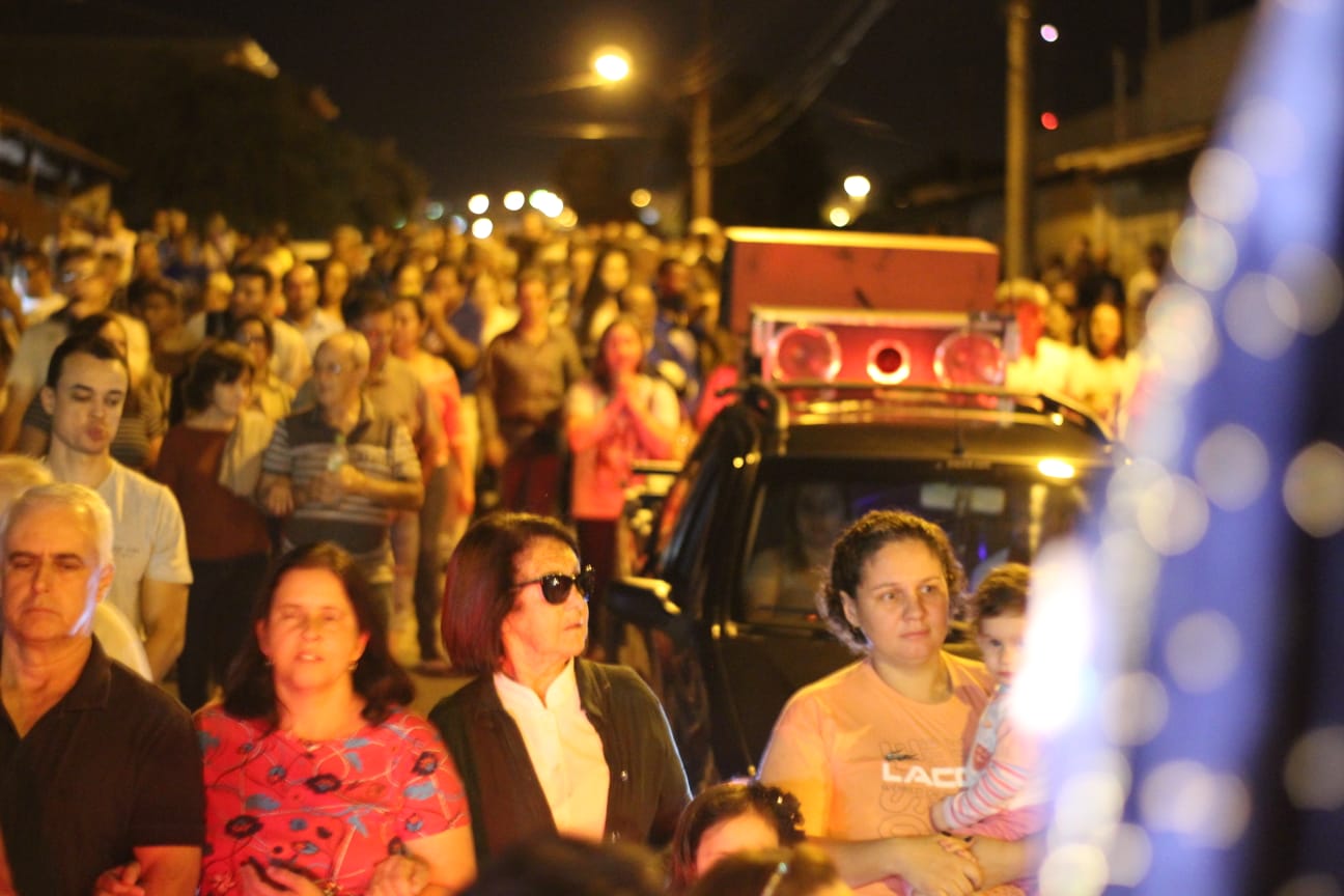Procissão noturna com fiéis acompanhando o carro de som